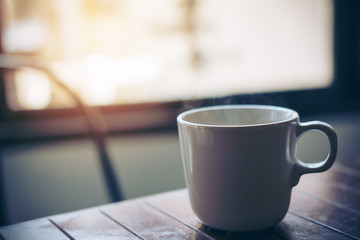 Closeup image of hot coffee cup on vintage wooden table in cafe