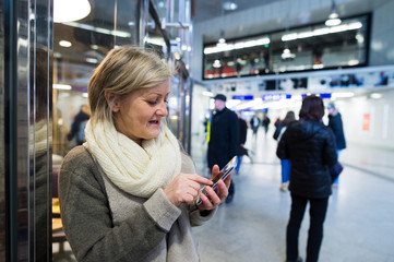 Fototapeta premium Senior woman with smartphone in hallway of subway