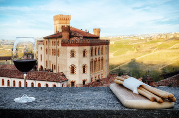 A chalice of Barolo red wine on a windowsill with breadsticks and the castle of Barolo (Piedmont, Italy) on the background - 141386908