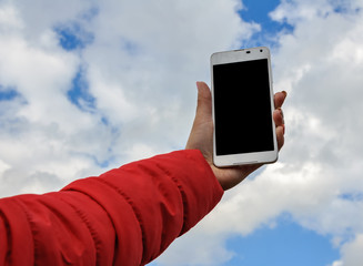 Woman hand holding smartphone against blue sky background