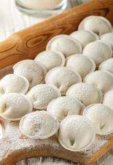Process of making homemade raw  dumplings with meat filling on a wooden Board. Pelmeni. A traditional dish of Russian cuisine. Selective focus
