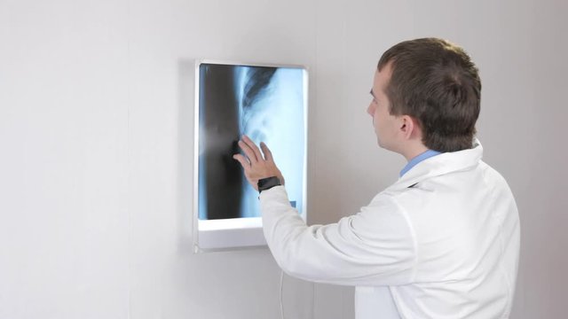The doctor examines the X-ray and drinks a hot drink. White wall and Nigatoscope with ribs and thorax