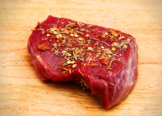 Top view of portion piece of raw meat with spices on wooden cutting board closeup for cooking steaks on the grill