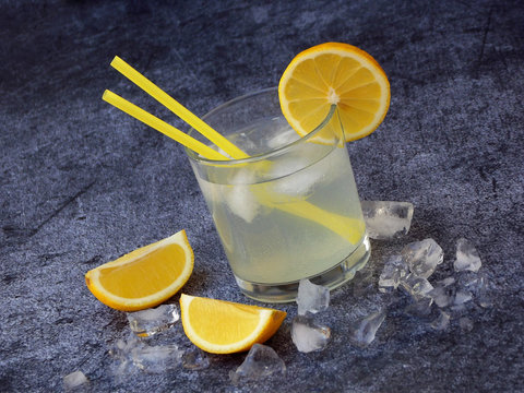 One glass of cold homemade lemonade with lemon slices, ice cubes and straws on dark background. Copy space
