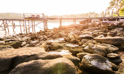 Rock beach and old wood bridge with sunset shading everithing to warm tone at kho kood thailand