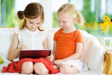 Two adorable little sisters playing with a digital tablet