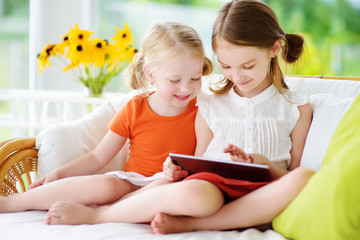 Two adorable little sisters playing with a digital tablet