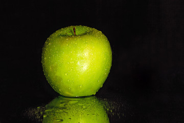 Close-up of a green apple with waterdrops on it and reflections below isolated on black.