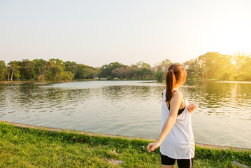 Happy successful sportswoman raising arms to the sky on golden back lighting sunset summer. Fitness athlete with arms up celebrating goals after sport exercising and working out outdoors. Copy space.