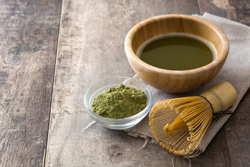 Matcha green tea in a bowl and bamboo whisk on wooden table
