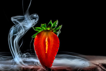 eine künstlerische Darstellung einer aufgeschnittenen Erdbeere vor schwarzem Hintergrund mit Nebel