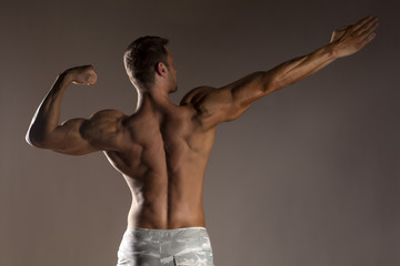 rear view of the half-naked handsome and muscular young man posing on a gray background