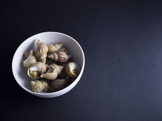 Whelks, sea snails, in white bowl isolated on black background