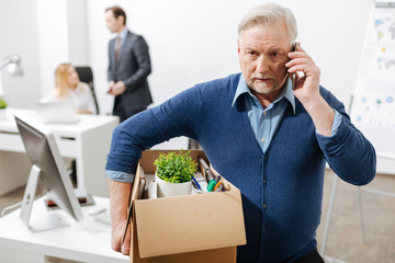 Puzzled old employee leaving office with the box full of belongings