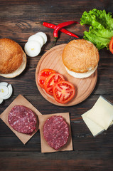 Homemade hamburger ingredients. Raw minced beef, fresh bun, slice of cheese, tomato, onion rings, lettuce on wood background