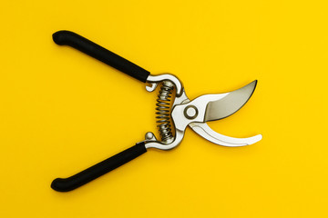 Metal secateurs isolated on a yellow background. Care of trees and bushes.