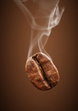 Closeup falling coffee bean with smoke on brown background
