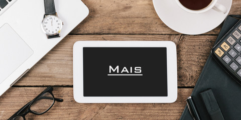 Naklejka premium Mais, Portuguese text for More on screen of tablet computer at office desk