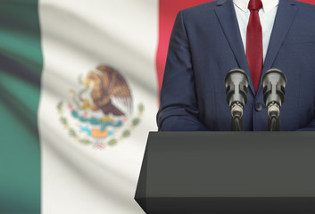 Businessman or politician making speech from behind a pulpit with national flag on background - Mexico