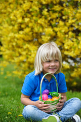 Funny  little boy with basket full of colorful easter eggs outdoors on a sunny day