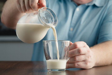 Man hand flowing milk from jar into glass