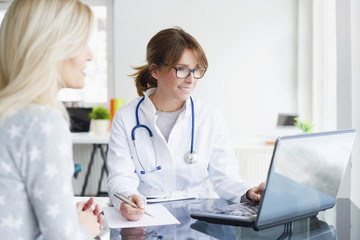 Doctor and her patient. Shot of a middle aged female doctor sitting in front of laptop and consulting with her patient.