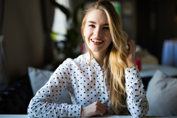 Beautiful blonde girl sitting in cafe over lights background.