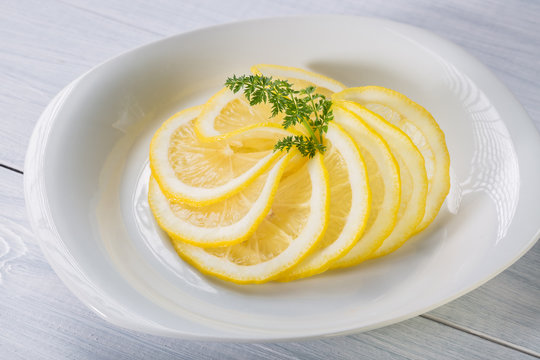 Sliced lemon pieces with herbs on white plate and white wooden table