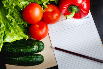 Fresh vegetables on the table: red pepper, lettuce, cucumber, tomatoes, sheet for notes - notepad. Cutting board