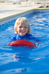 Fototapeta na wymiar Happy little boy with floating board in swimming pool
