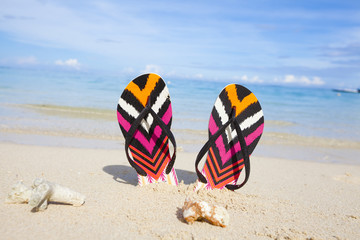 Colorful flip-flops stuck in the sand on tropical beach with turquoise ocean in the background