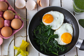 fried eggs on spinach in a frying pan with cress, broken shells on the side, on white board