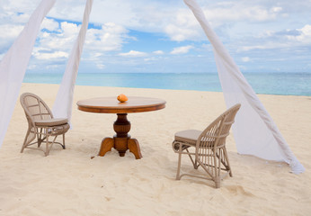 Private dining table and wicker chairs for romantic dinner for honeymoon couples on a tropical beach