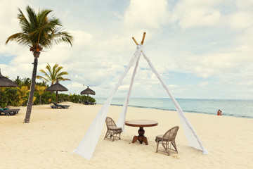 Private dining table and wicker chairs for romantic dinner for honeymoon couples on a tropical beach