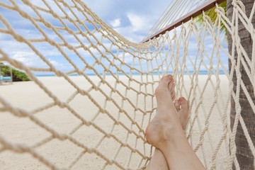 Female legs on hammock on tropical beach with palm palm trees in the background