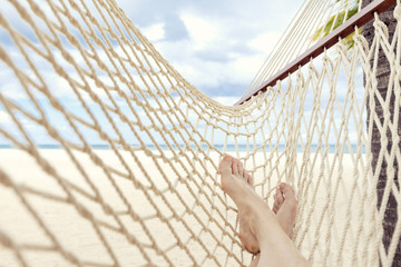 Female legs on hammock on tropical beach with palm palm trees in the background