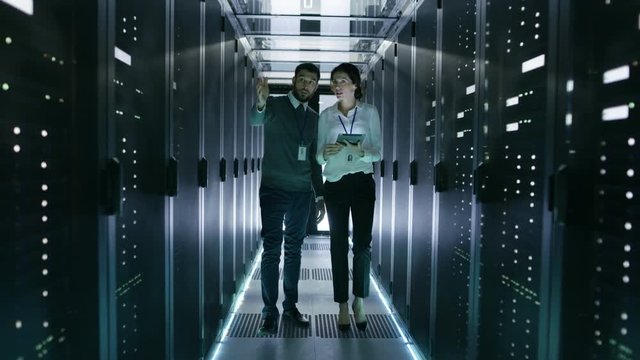 In Data Center/ Server Room IT Engineer Consults with Female Chief Engineer who Holds Tablet Computer. Shot on RED EPIC-W 8K Helium Cinema Camera.