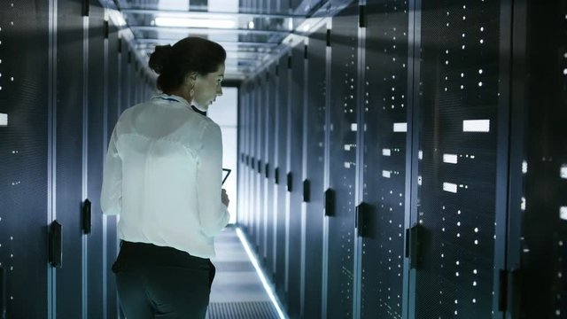 Female Server Technician Walking in Data Center Corridor with Rows of Rack Servers. She's Running Diagnostics on Her Tablet Computer. Shot on RED EPIC-W 8K Helium Cinema Camera.