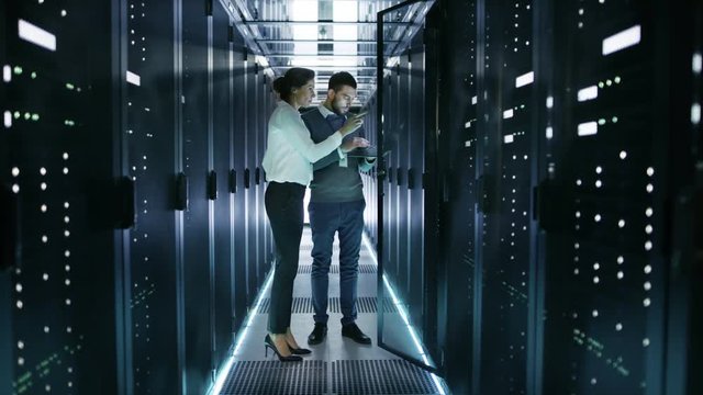 Female IT Technician and Male Server Engineer Discussing Settings of a Working Data Center. Man Holds Laptop They Stand Before Open Rack Server. Shot on RED EPIC-W 8K Helium Cinema Camera.