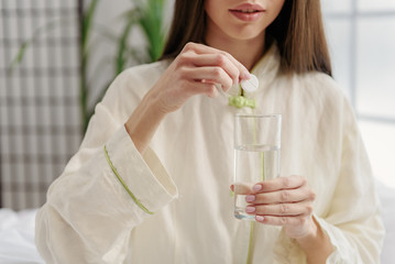 Calm young female putting pill in glass of water