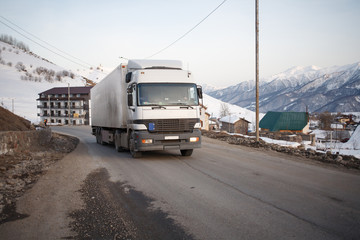 Obraz premium White refrigerated truck on winter road on background of the mountains