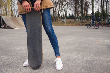 Portrait of of a young happy girl holding a skateboard. Skate park cyclist in the background.