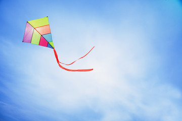 angle view of a colorful kite flying with waving red bow in a deep blue sky with the light of the...