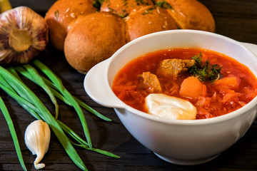 Traditional Ukrainian soup borscht with savory garlic bun pampushkas on the table among vegetables and spices