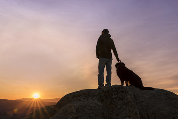 Man and his faithful companion watching the sunrise on top of the mountain - obrazy, fototapety, plakaty
