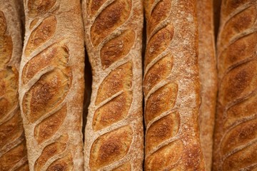 Overhead closeup macro of neatly stacked rustic fresh golden French bread loaf row with cracked crispy crust dusted with baking flour at organic local farmers market bakery
