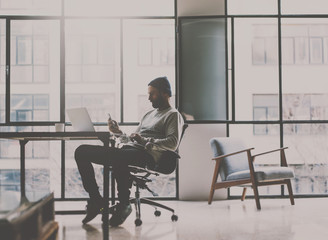 Bearded coworker man relaxing in chair at modern coworking studio and using smartphone.Panoramic windows on blurred background.Horizontal.