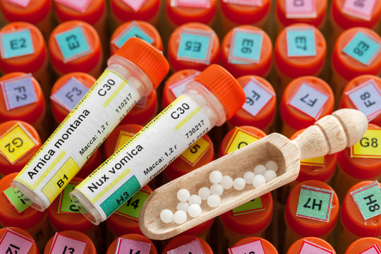 Tubes of homeopathy globules, scoop  and list of different homeopathic preparation of first aid kit on background.