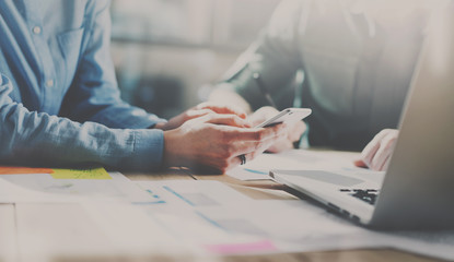 Concept of business teamworking.Young coworkers team working with new startup project in modern office.Mobile smartphone holding female hands. Horizontal, blurred background.