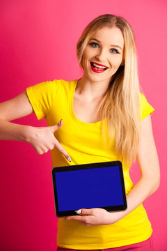 Beautiful blonde teenage woman pounting in blank tablet as advertisement over pink background